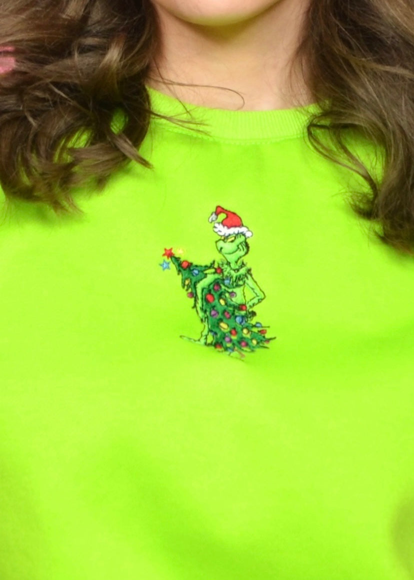 Close-up of playful green hand stealing decorated tree embroidery on lime-green holiday sweatshirt.