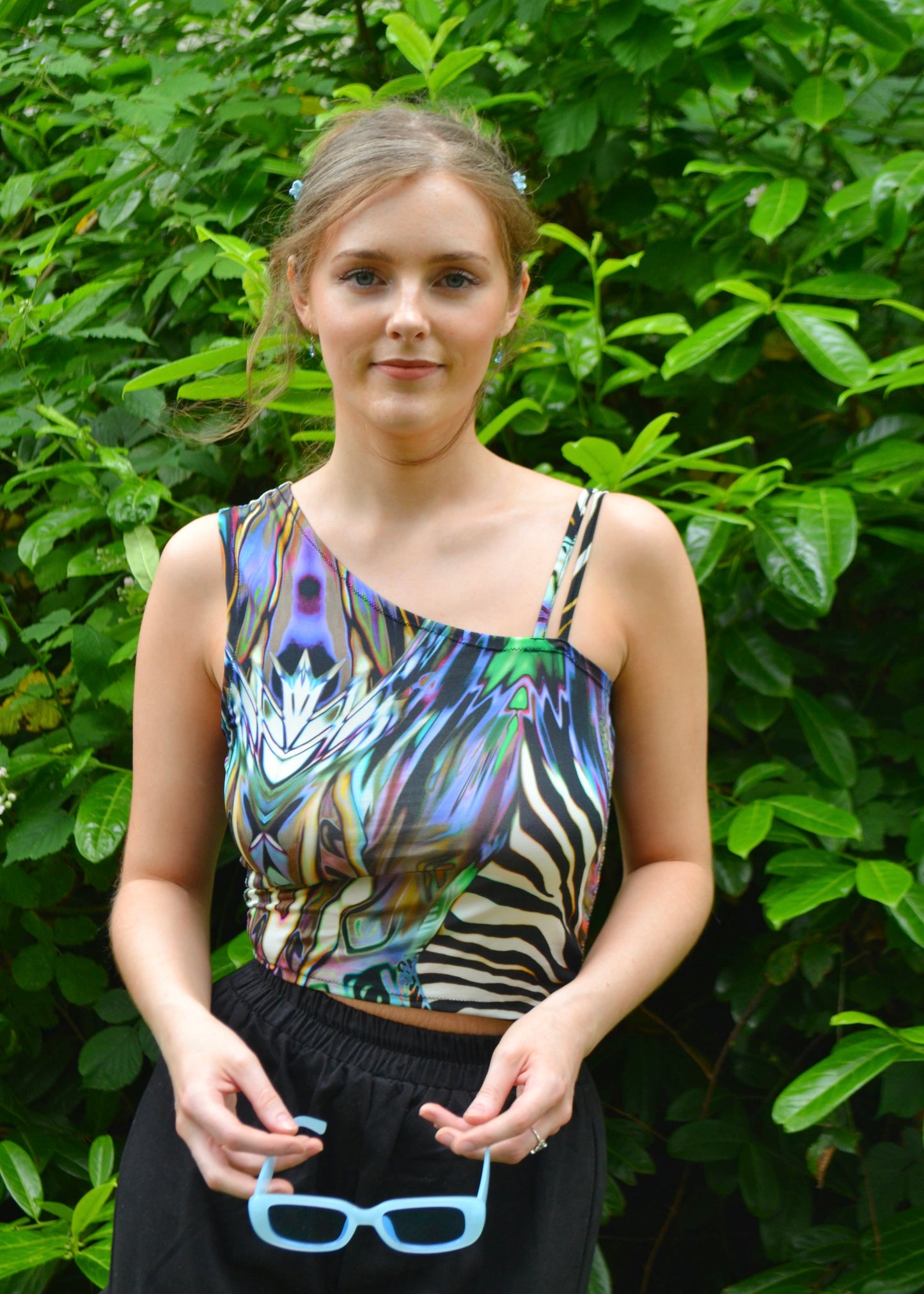 Model holding blue sunglasses, showing asymmetric neckline of handmade animal-print top