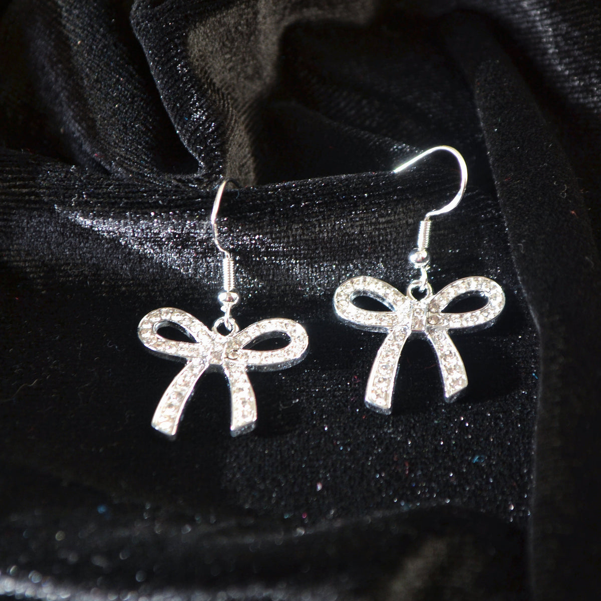 Silver bow-shaped earrings on a black velvet background