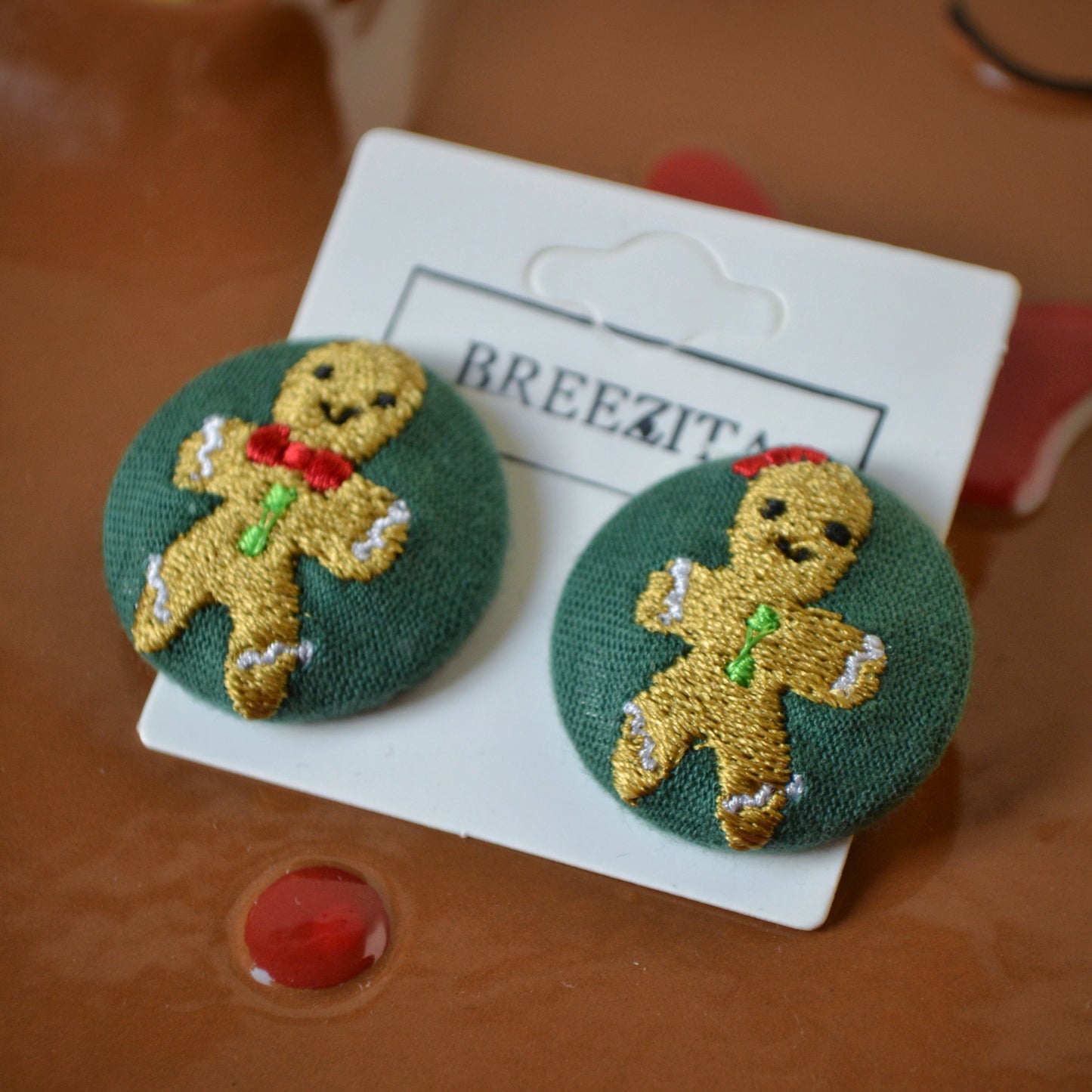 Gingerbread-themed earrings on a Breezita card against a brown background