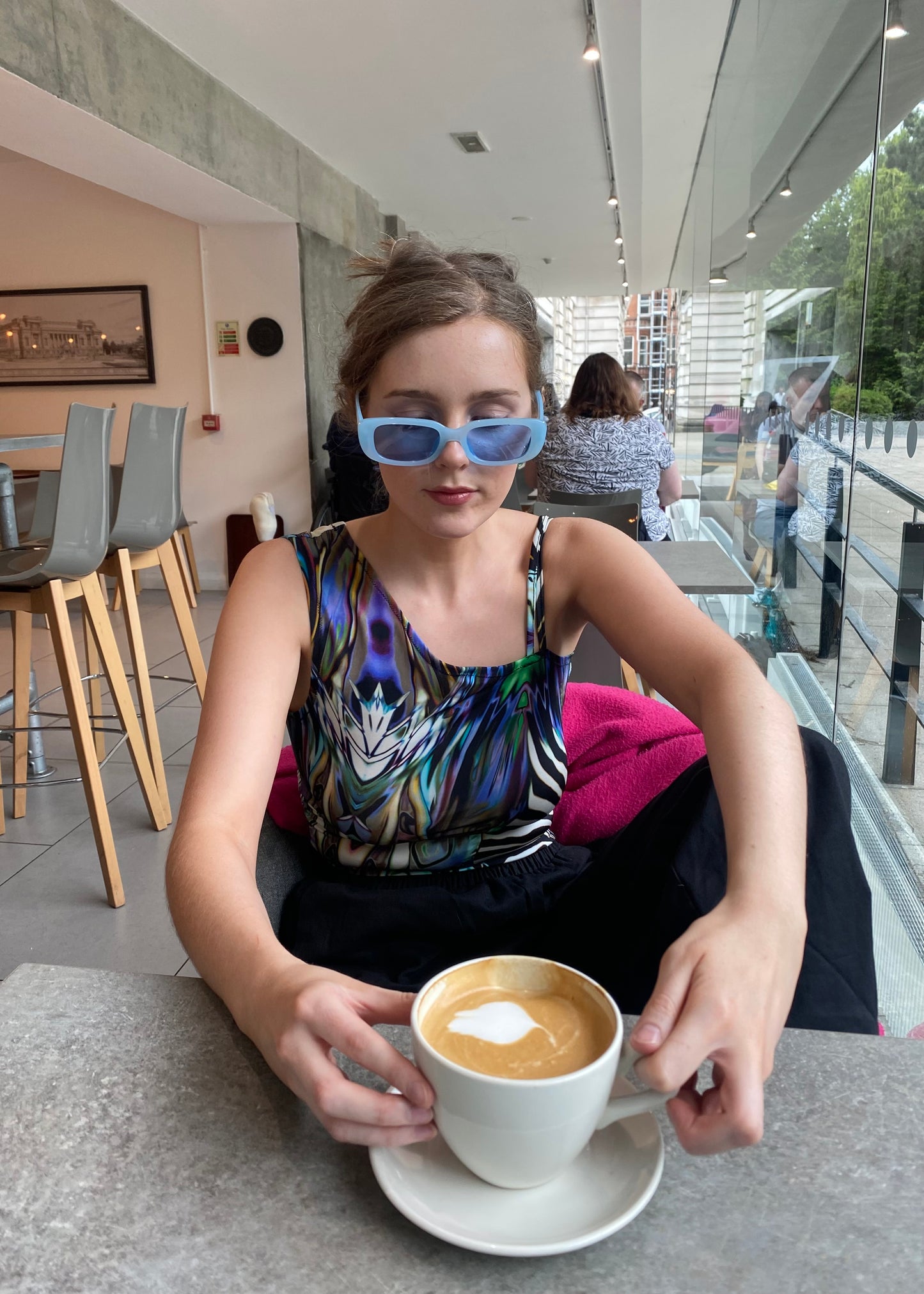 Model wearing handmade one-shoulder animal-print top sipping latte in modern café