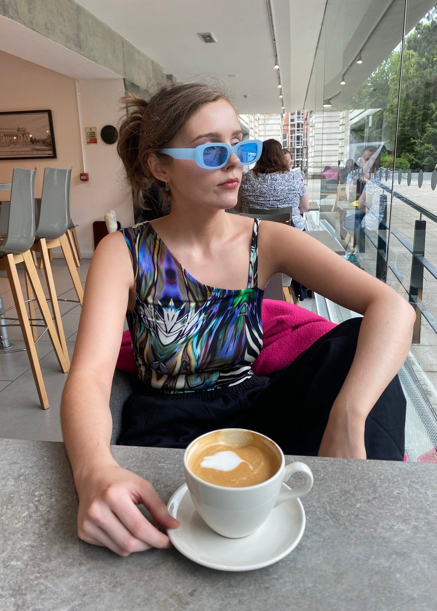 Side view of model in handmade animal-print festival top and blue sunglasses in café