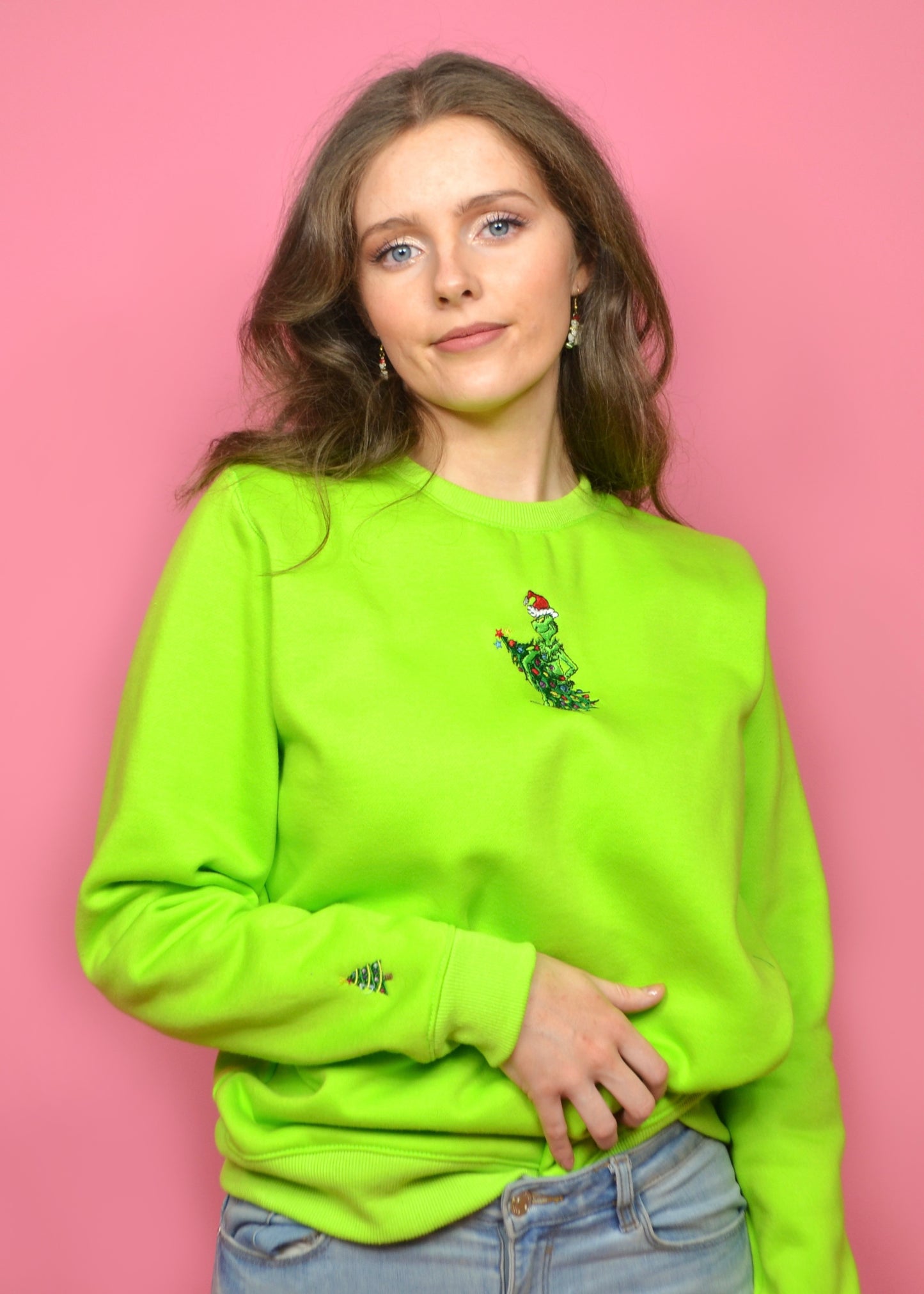 Three-quarter pose: lime-green festive sweatshirt with cheeky tree-steal embroidery, model hand on waist