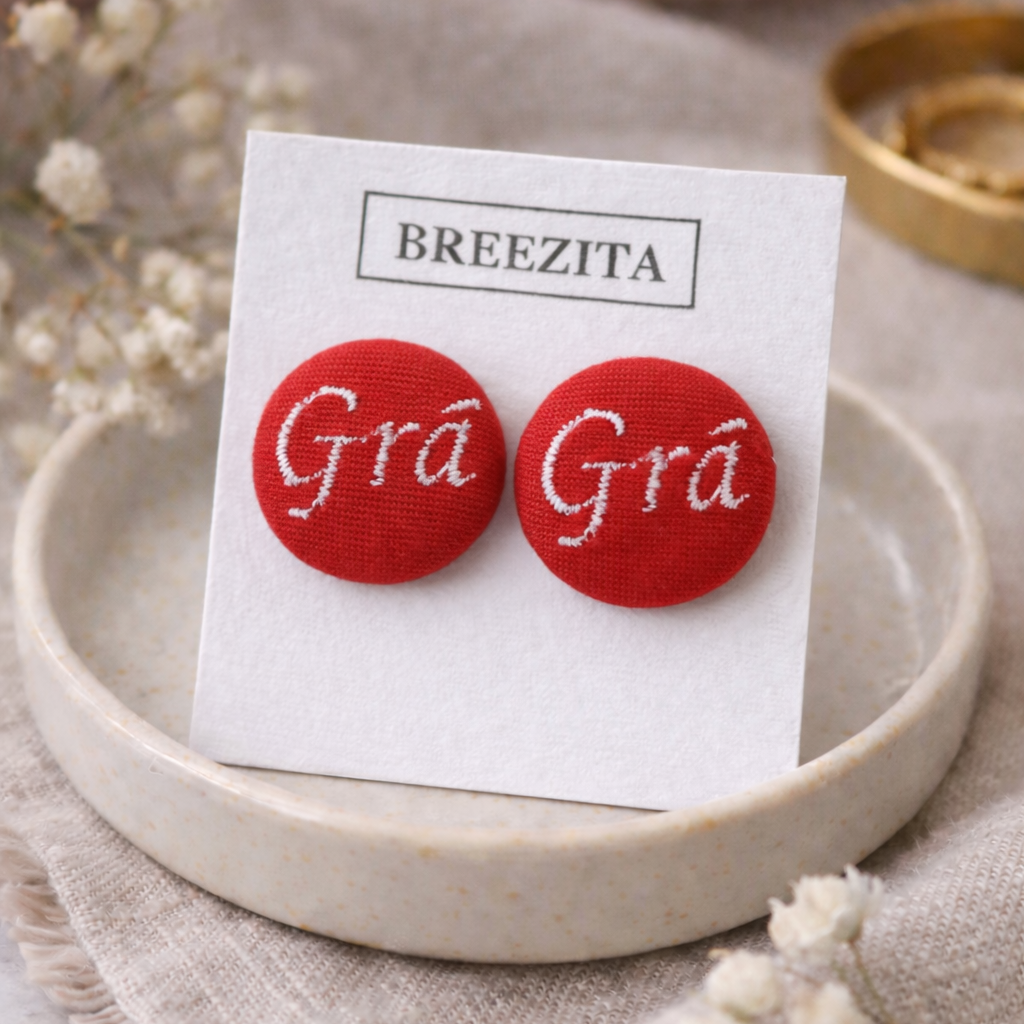 Red earrings with 'Grá Grá' text on a Breezita card, displayed on a beige plate.