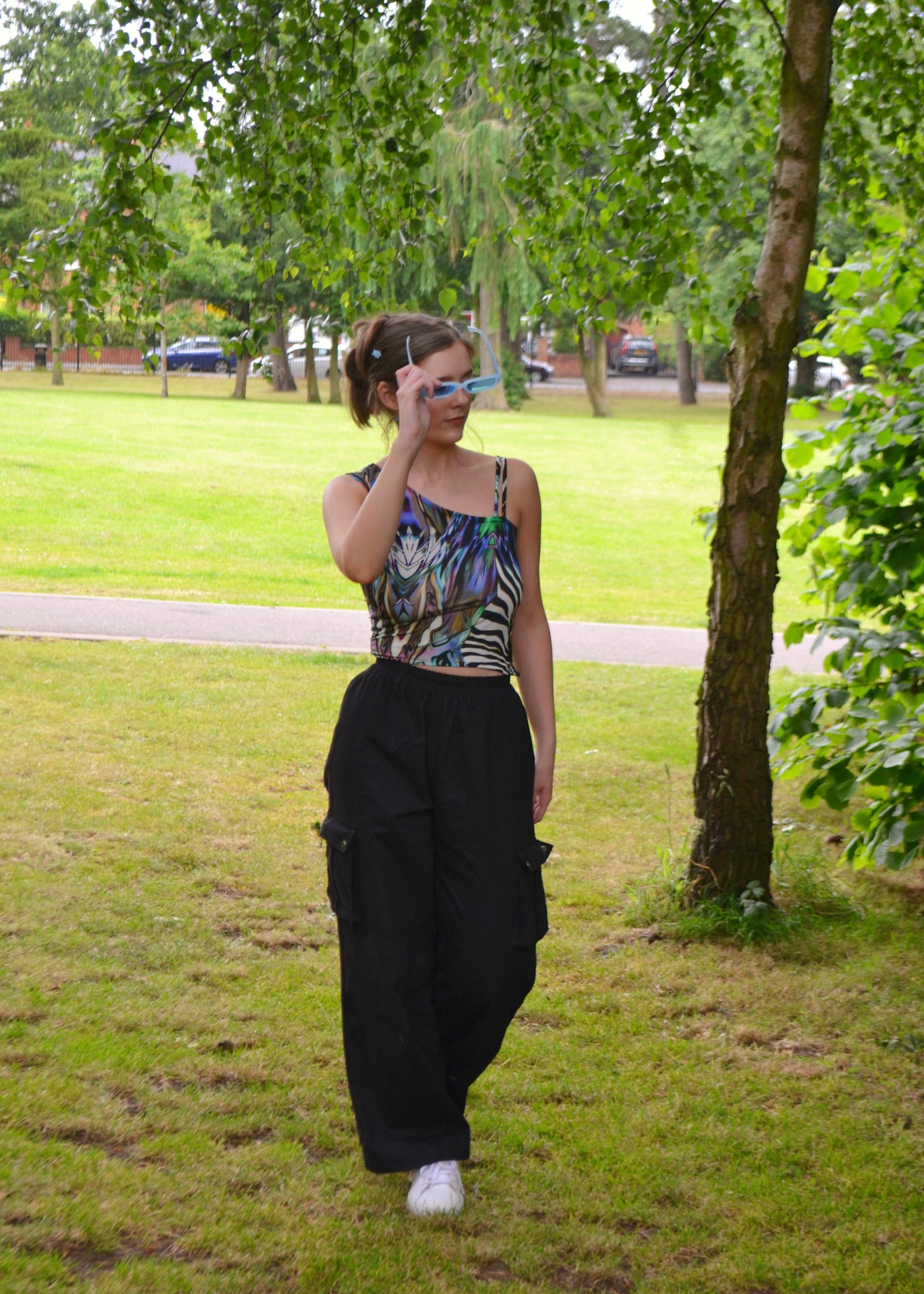 Full-body shot walking in park wearing handmade animal-print festival top with cargo pants
