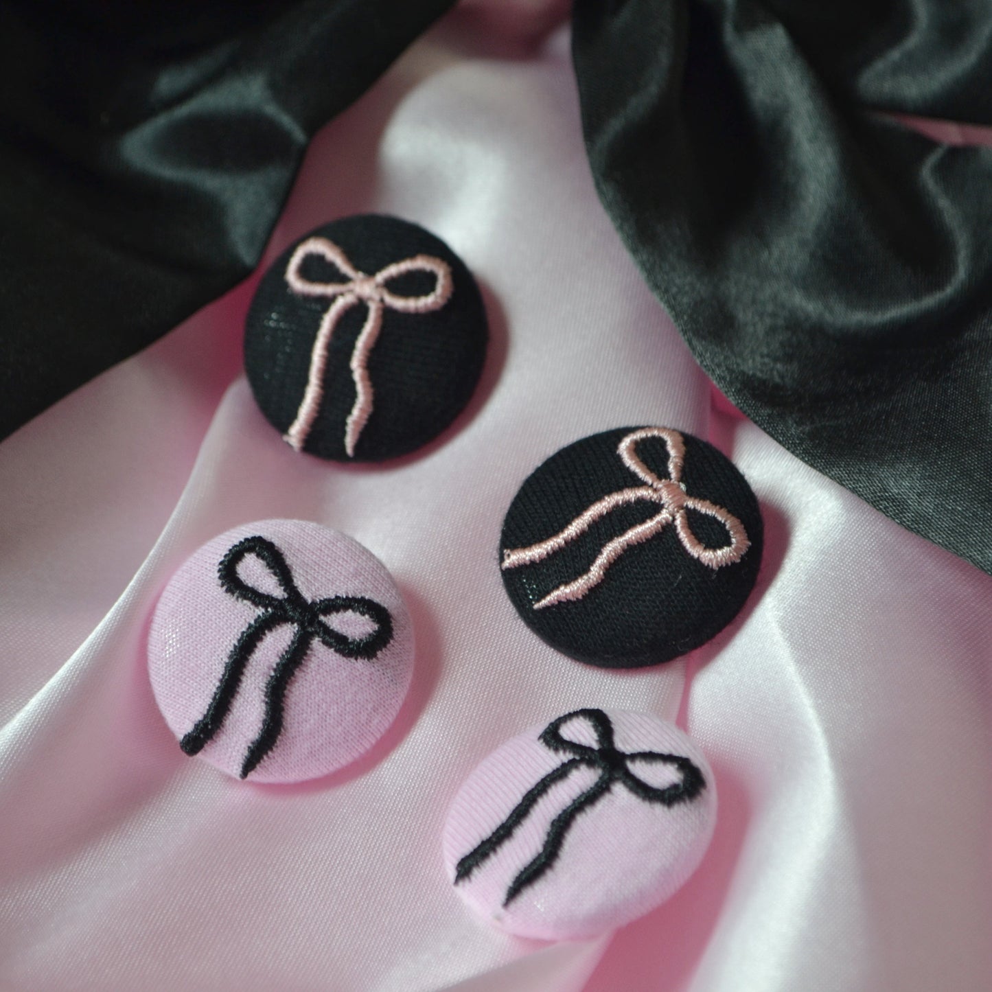 Four fabric buttons with embroidered bows on a satin surface