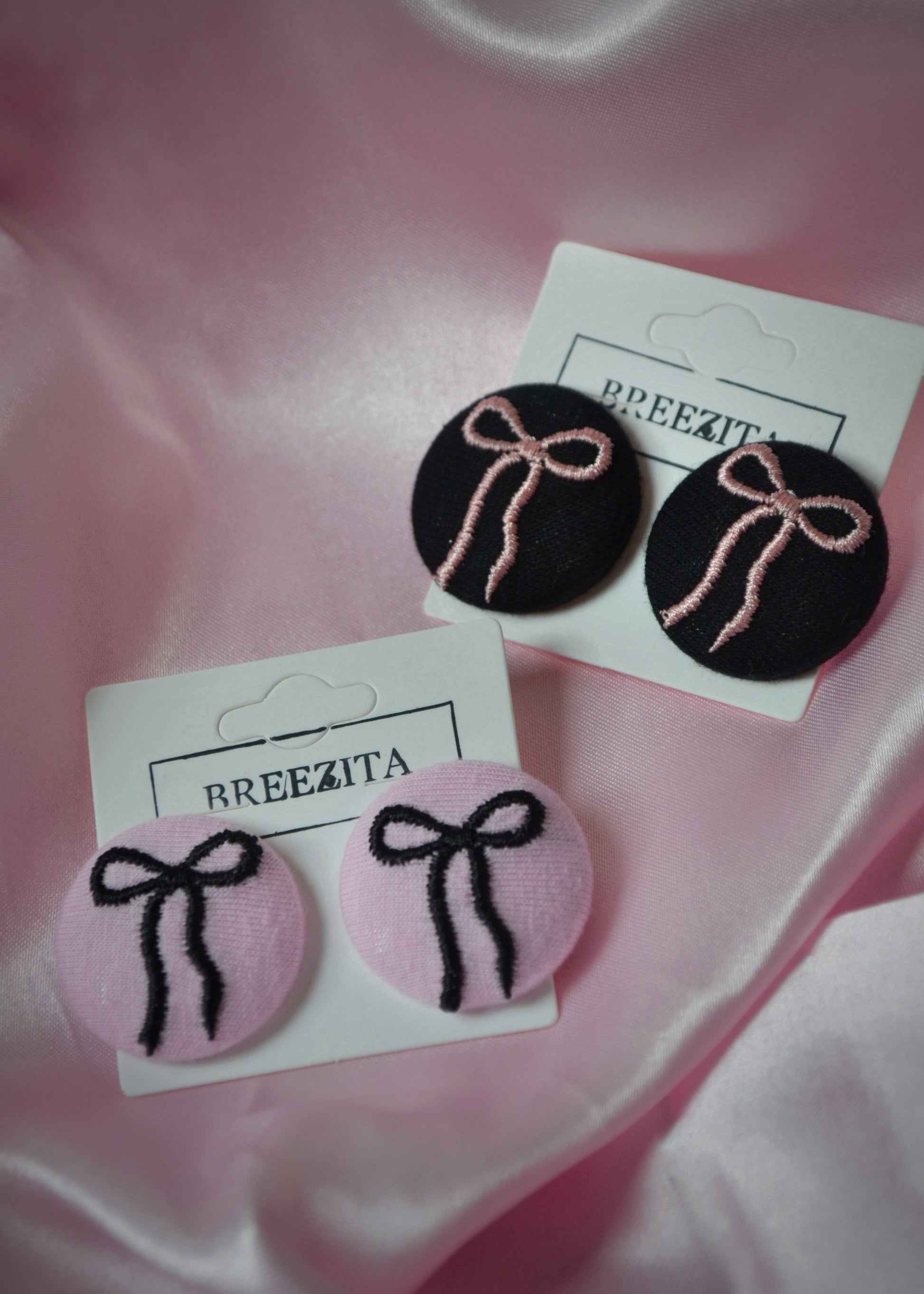 Pair of earrings with pink and black bows on a pink satin background