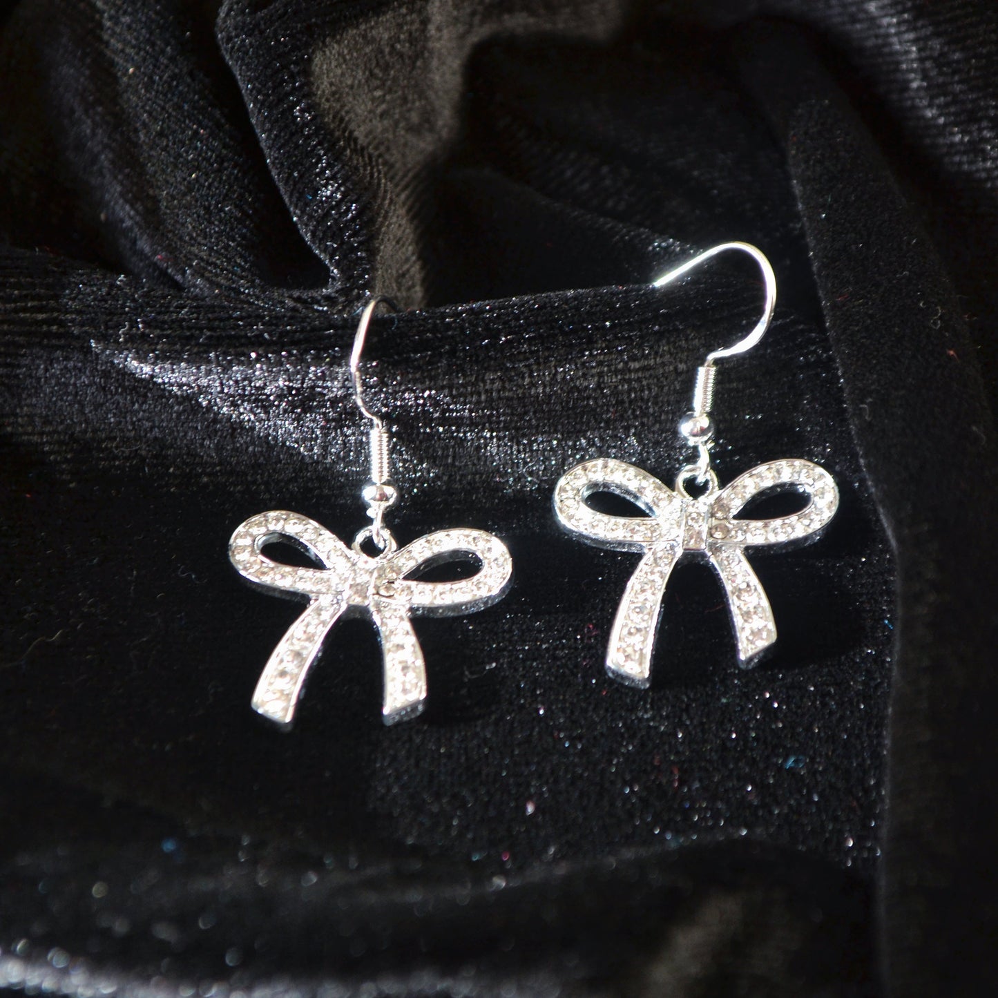 Silver bow-shaped earrings on a black velvet background
