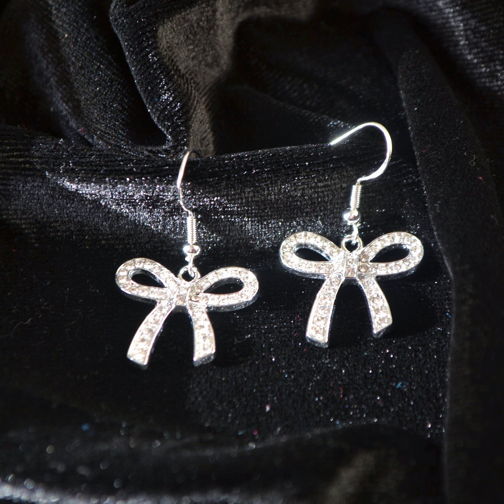 Silver bow-shaped earrings on a black velvet background
