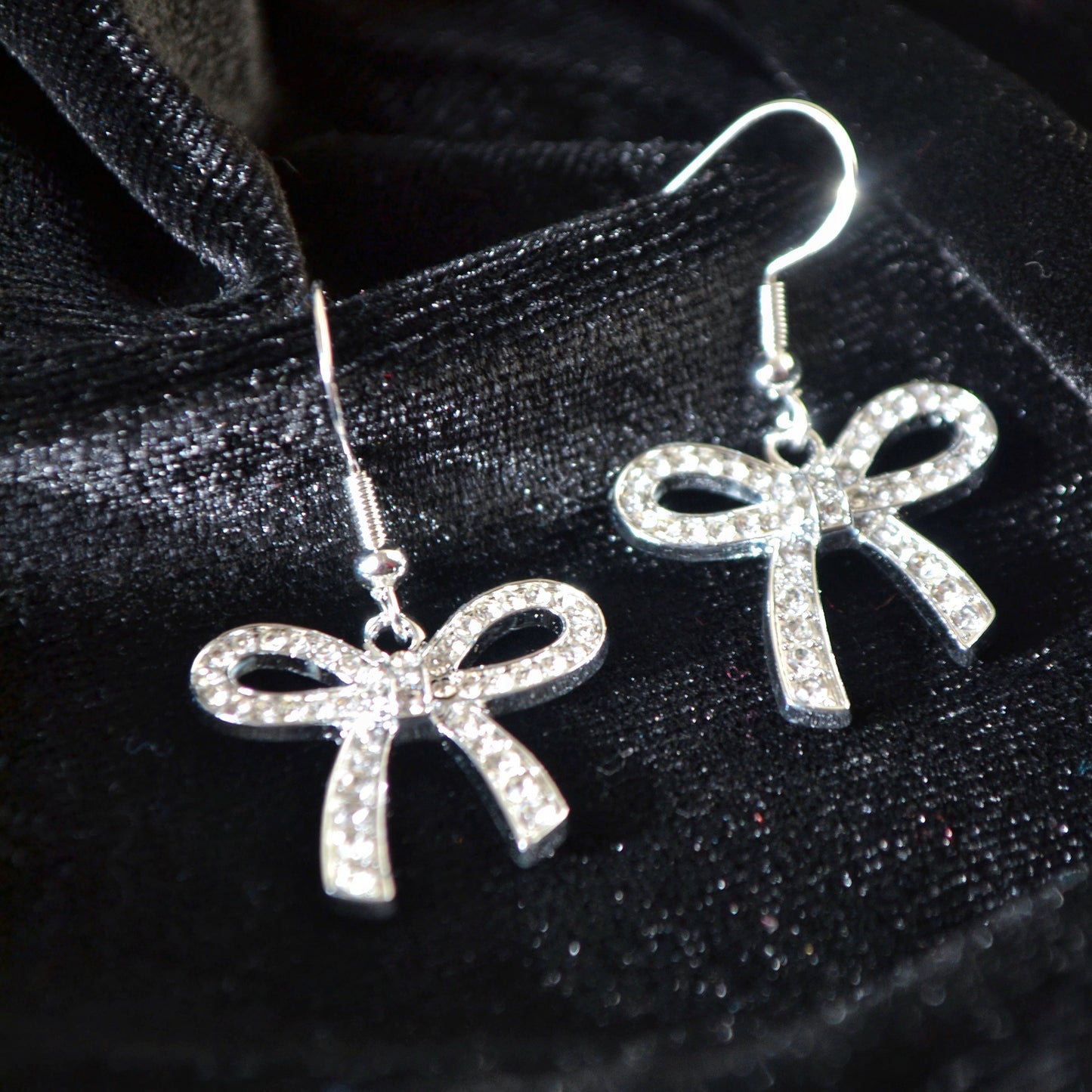 Silver bow-shaped earrings on a black satin background