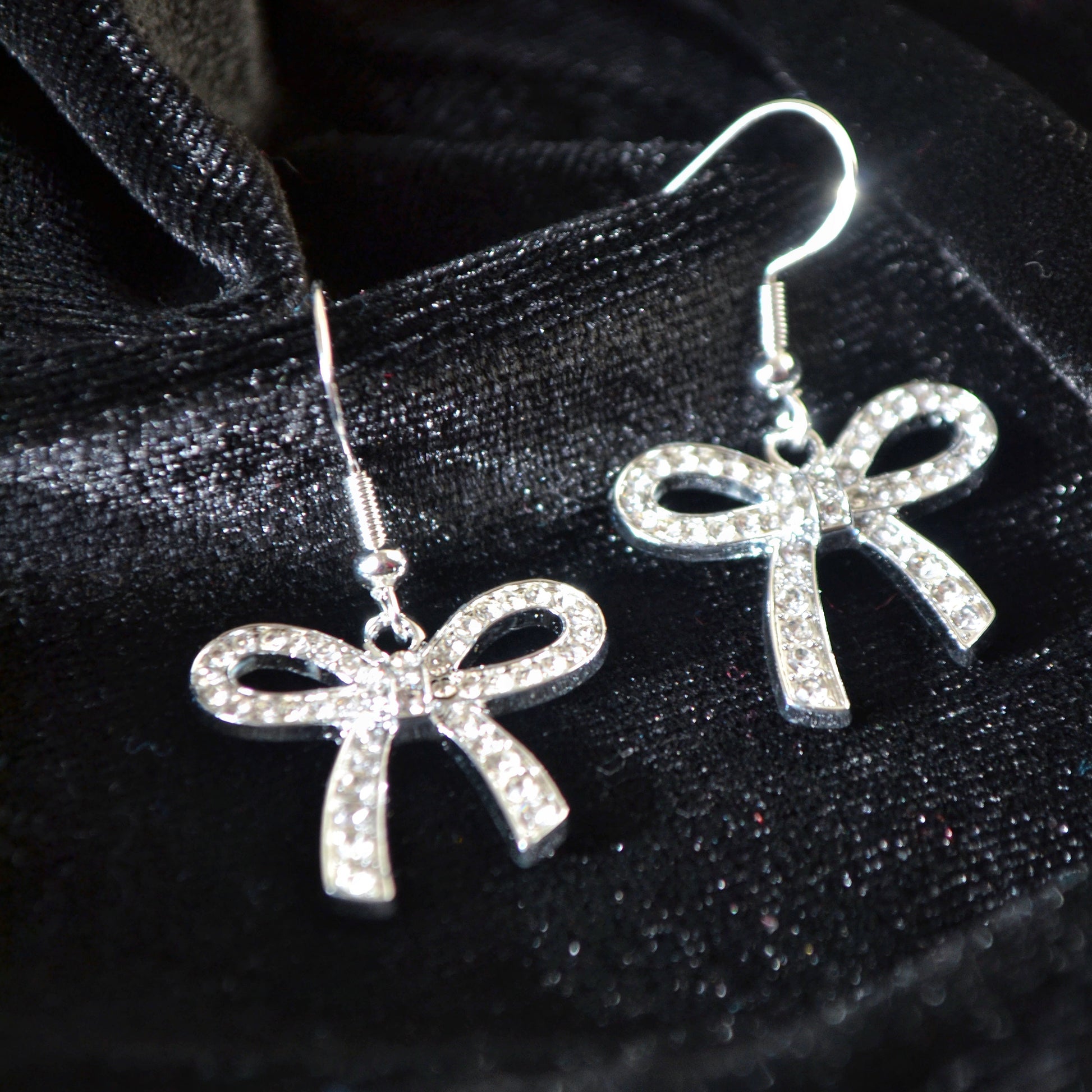 Silver bow-shaped earrings on a black satin background