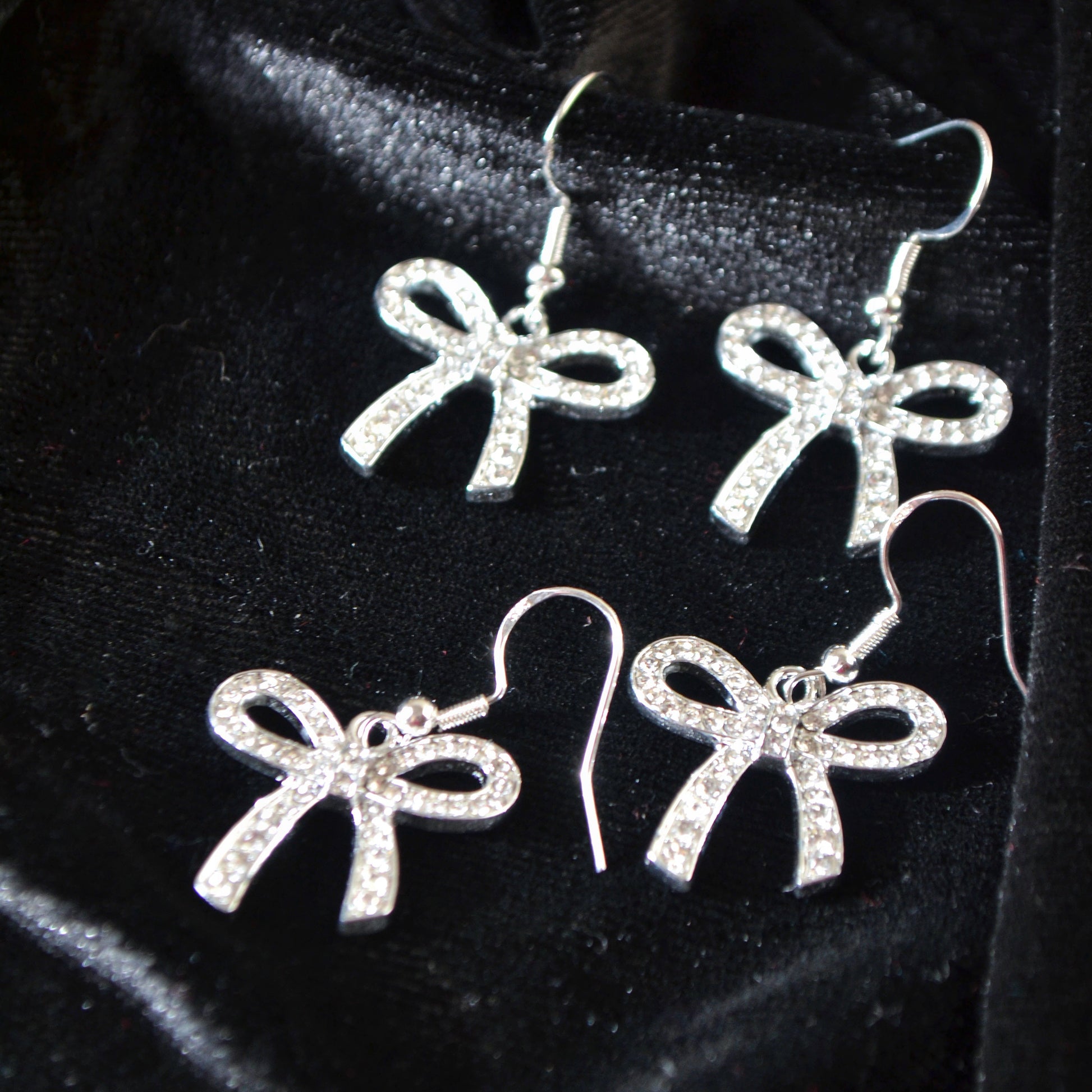 Silver bow-shaped earrings on a black velvet background