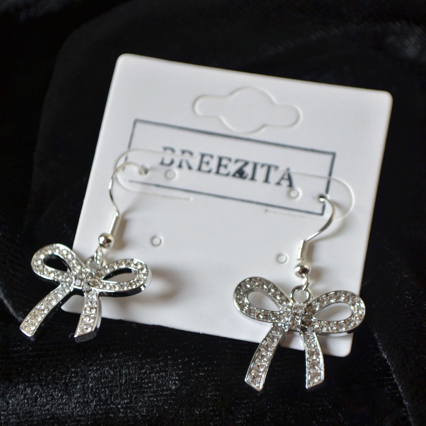 Bow-shaped earrings on a Breezita branded card against a dark background