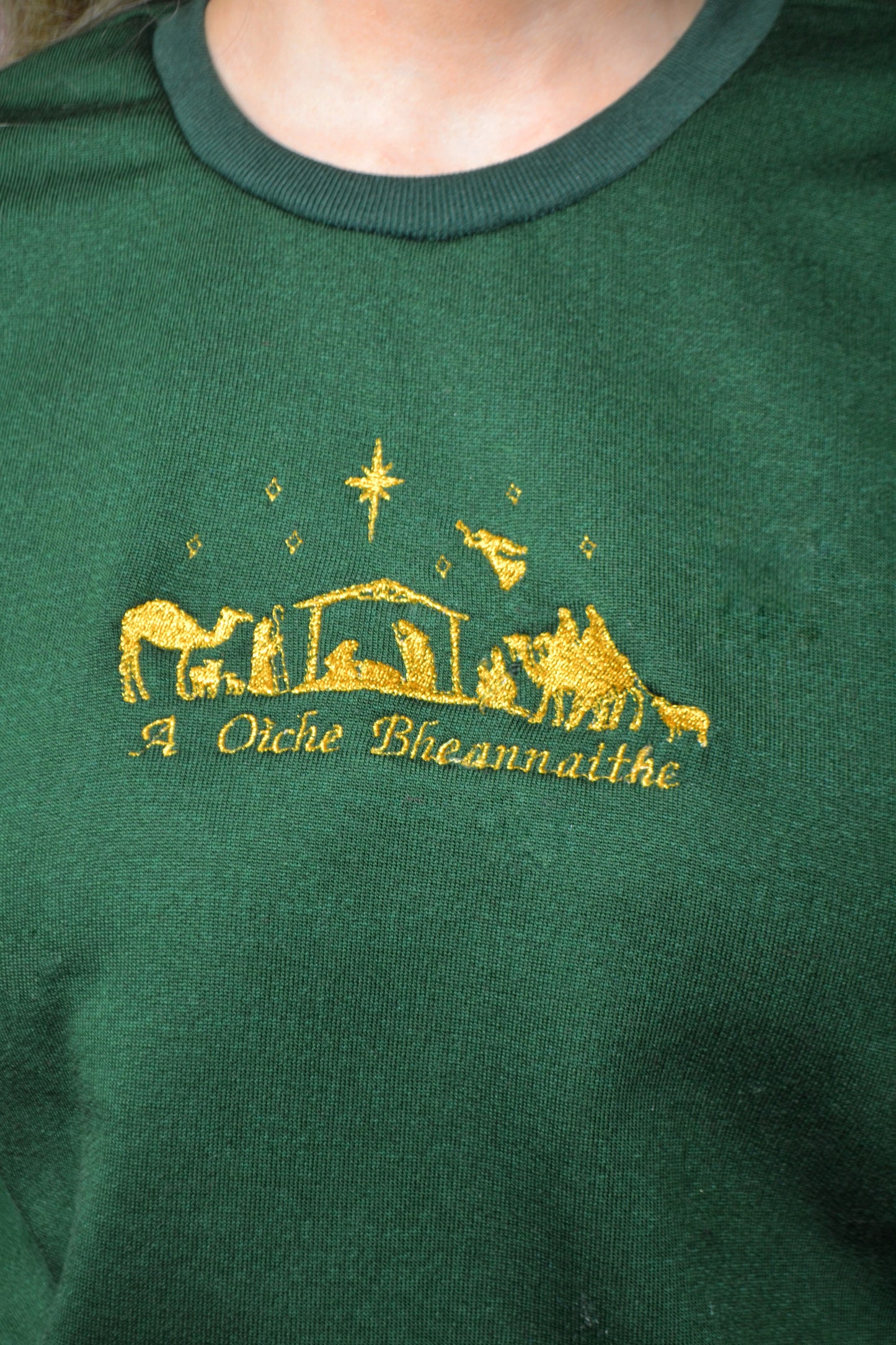Green sweater with gold nativity scene design and Irish text