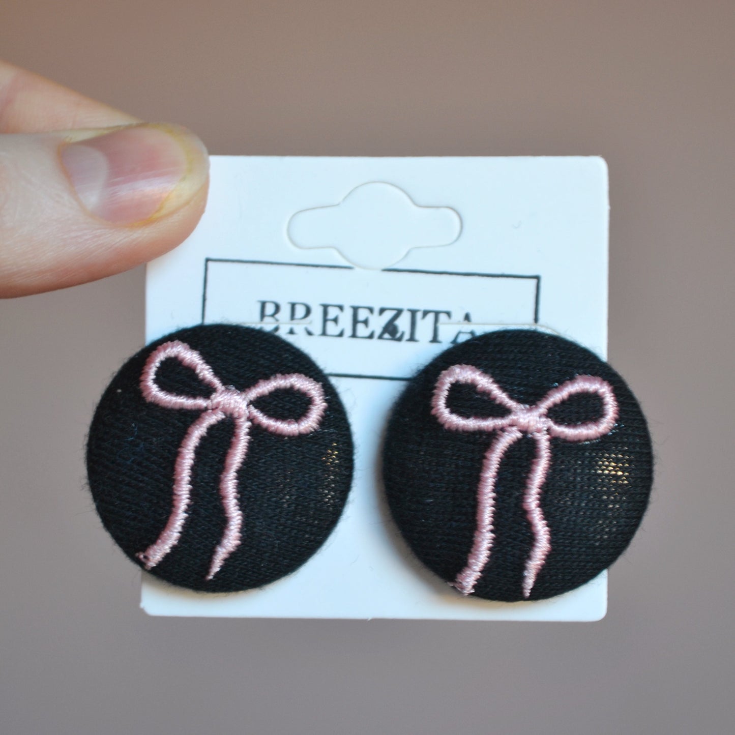 Black earrings with pink bows on a Breezita card against a pink background