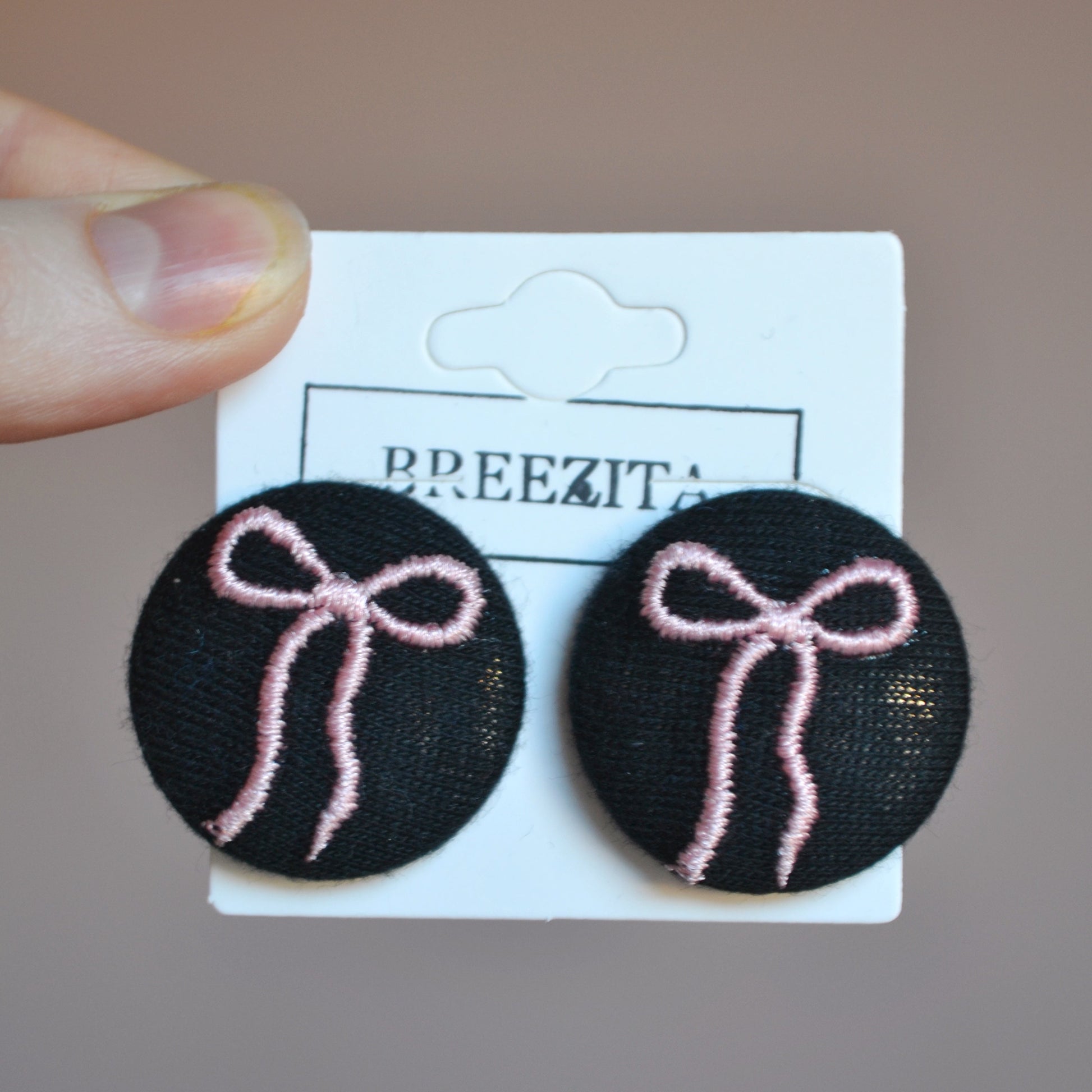 Black earrings with pink bows on a Breezita card against a pink background