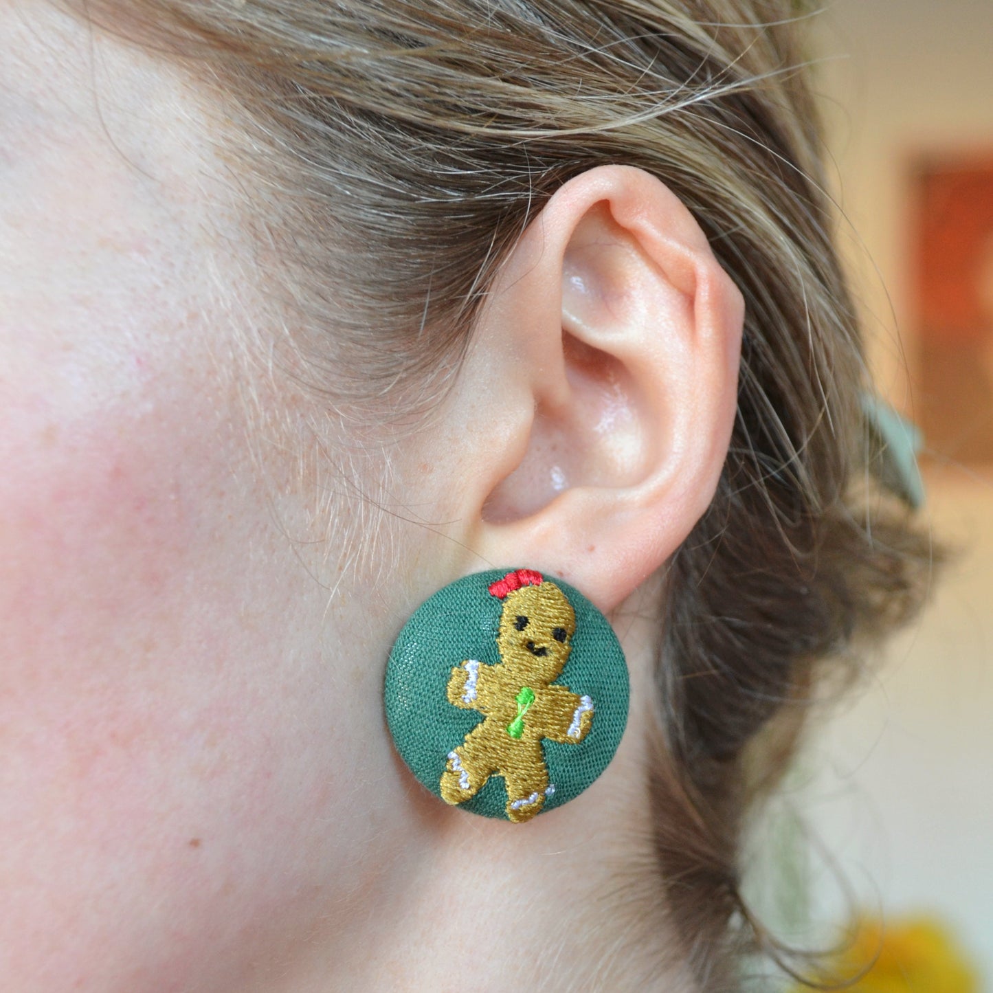 Close-up of a person wearing a green earring with a gingerbread man design.