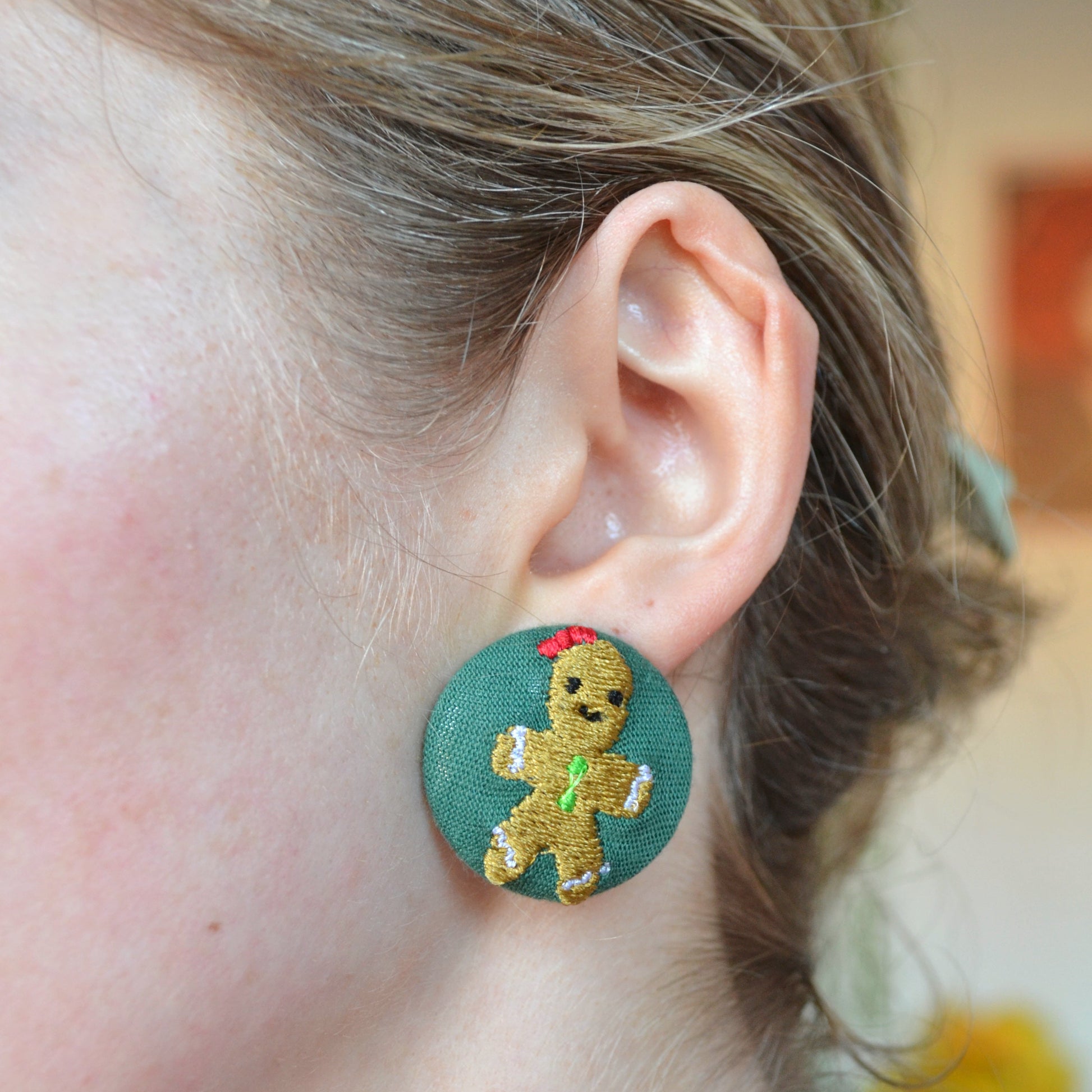 Close-up of a person wearing a green earring with a gingerbread man design.