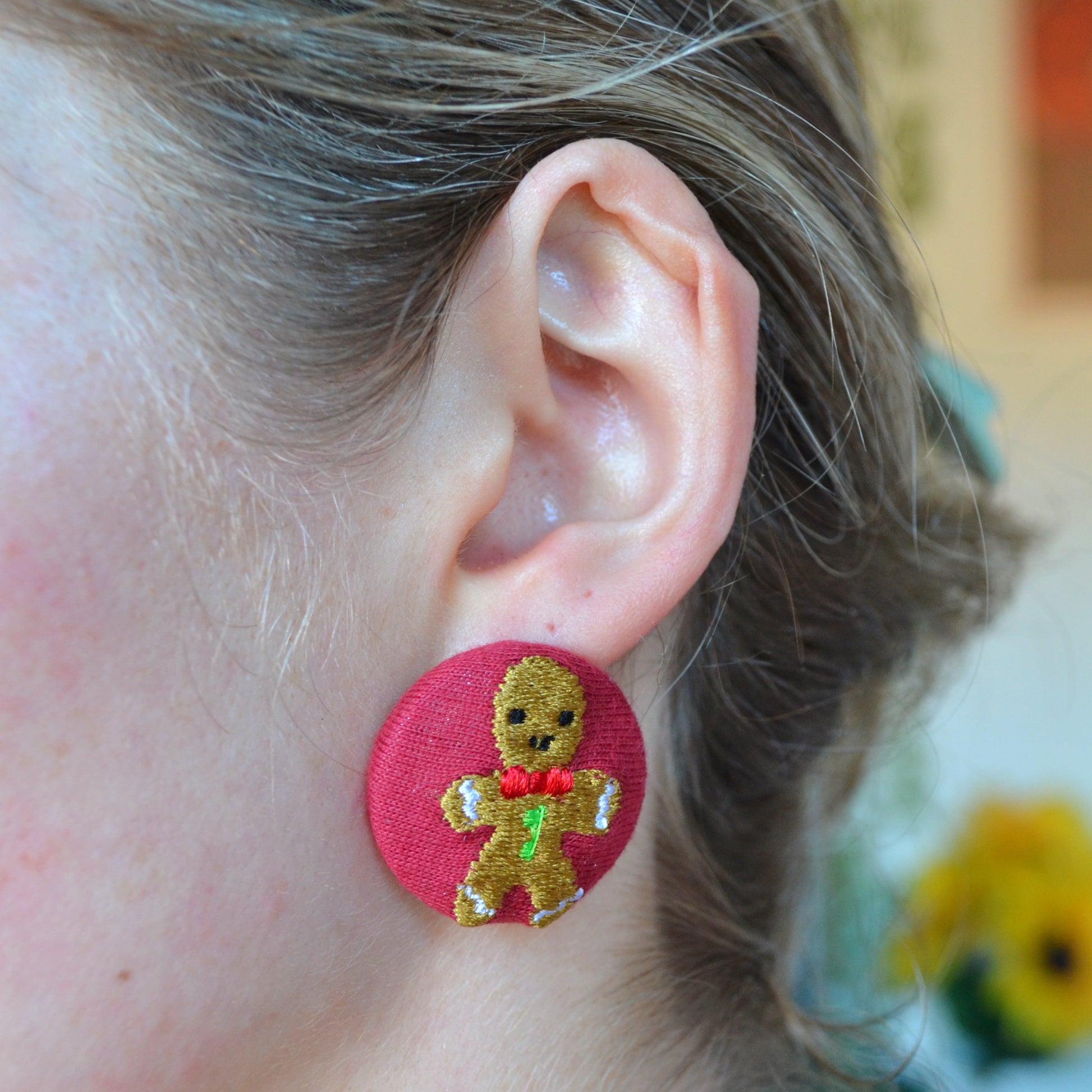 Close-up of an ear wearing a round red earring with a gingerbread man design.