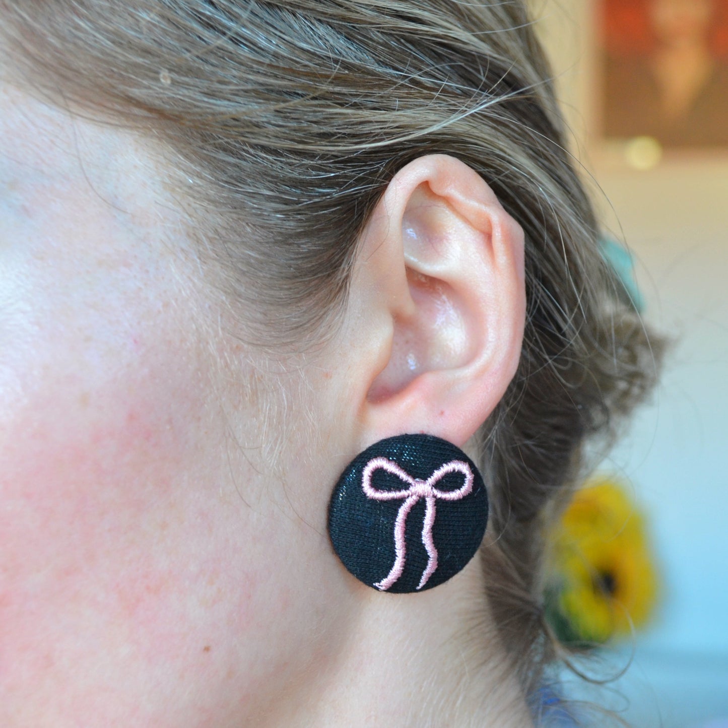 Close-up of an ear wearing a black earring with a pink bow design, blurred background