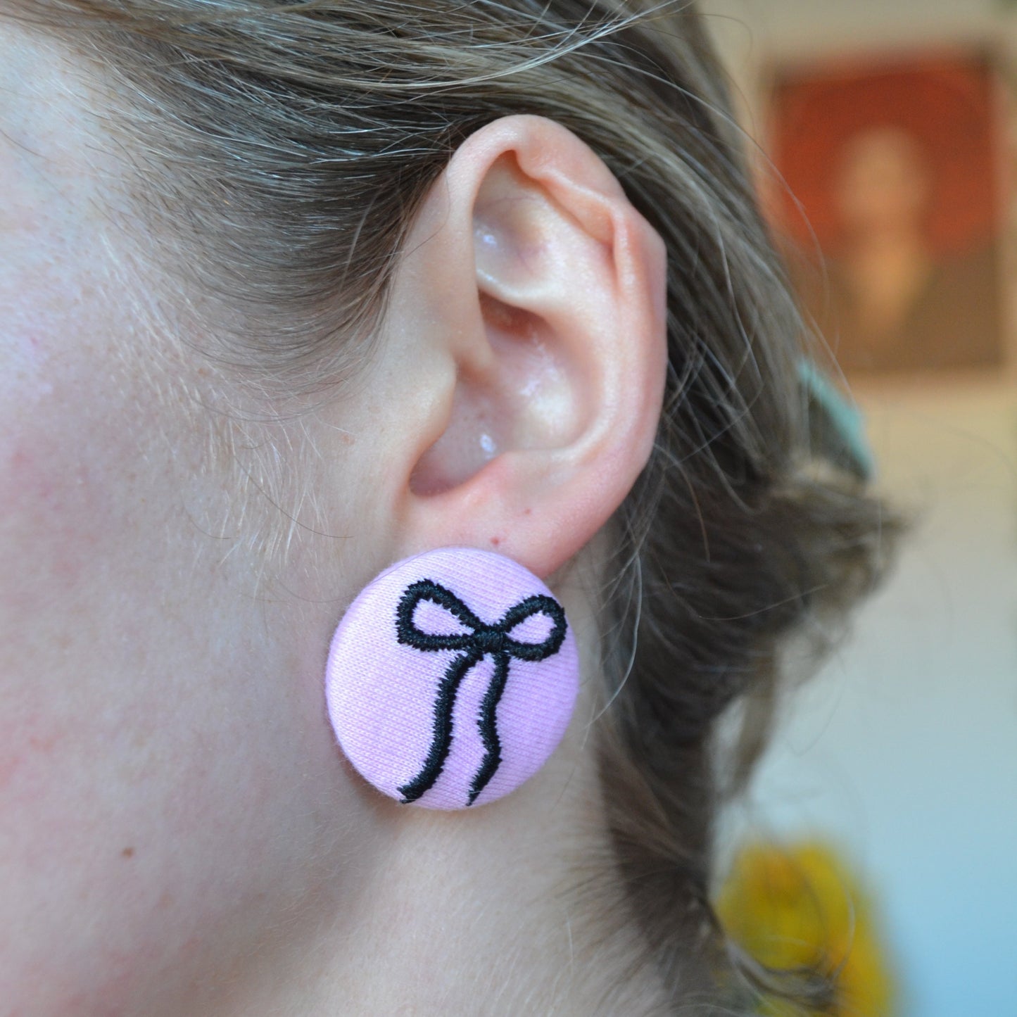 Close-up of an ear wearing a pink earring with a black bow design.