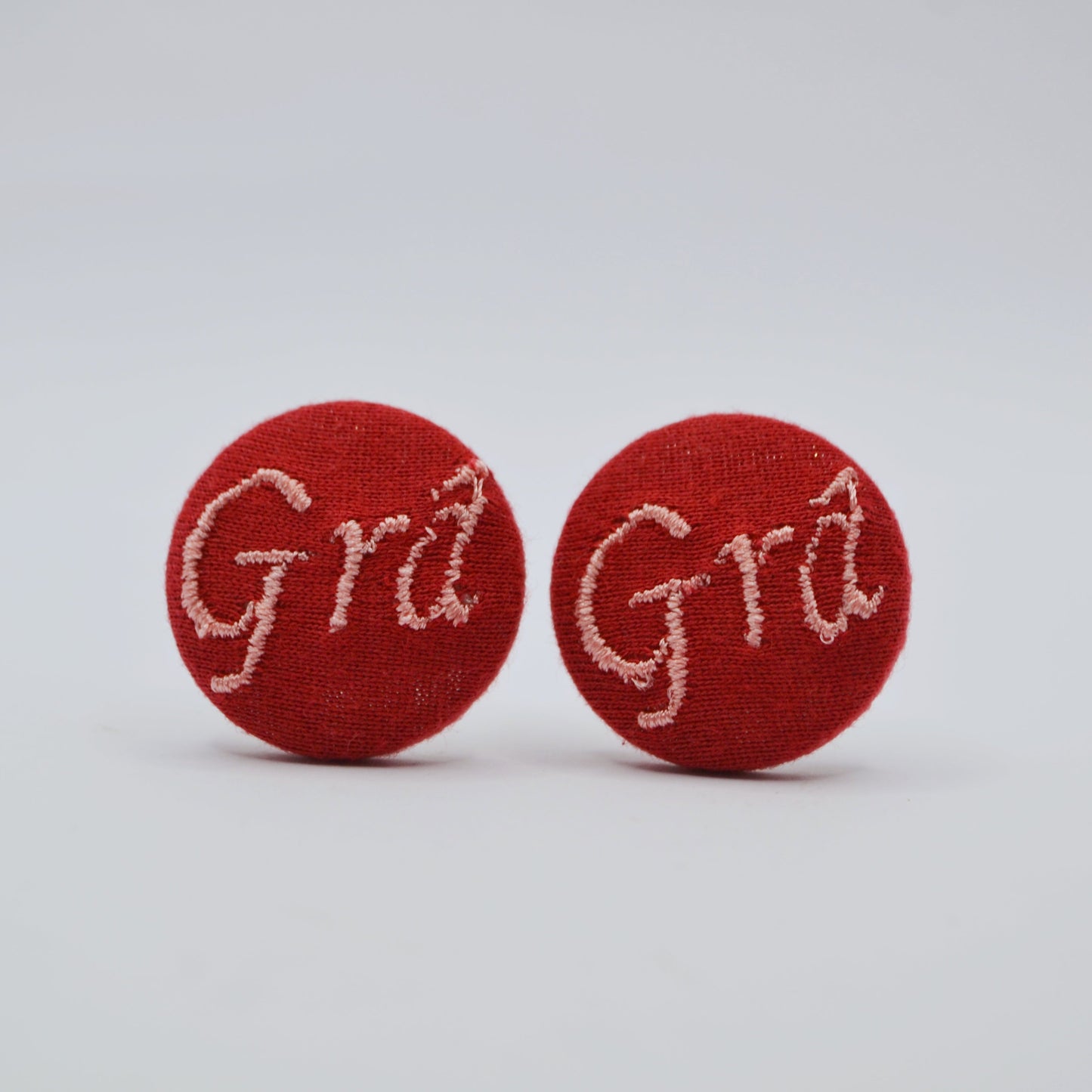 Maroon earrings with pink 'Grá' text on a light gray background