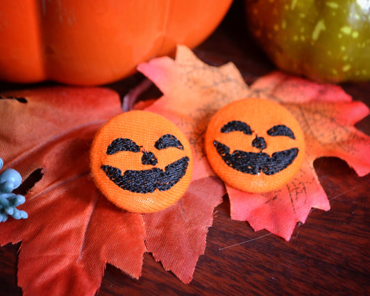 Cute Halloween pumpkin earrings with smiling faces, handmade fall accessories on rustic autumn leaves