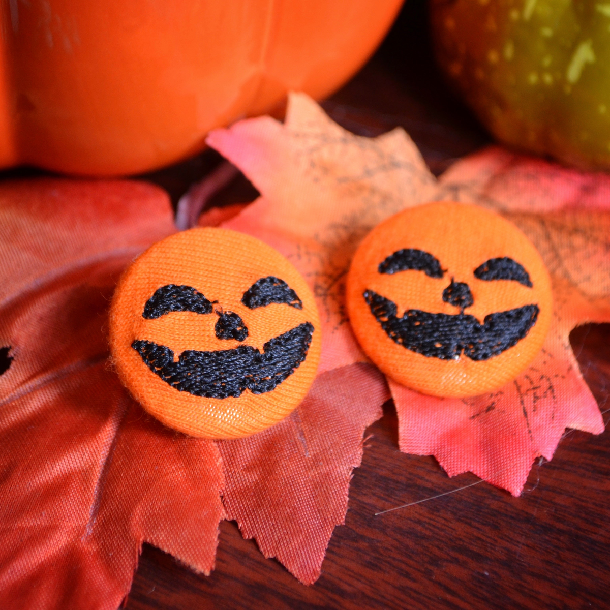 Cute Halloween pumpkin earrings with smiling faces, handmade fall accessories on rustic autumn leaves