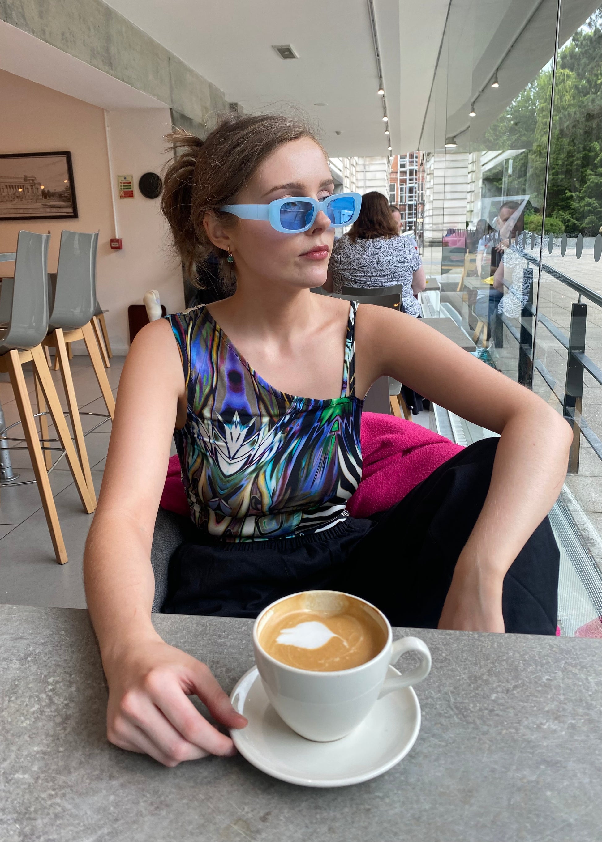 Side view of model in handmade animal-print festival top and blue sunglasses in café