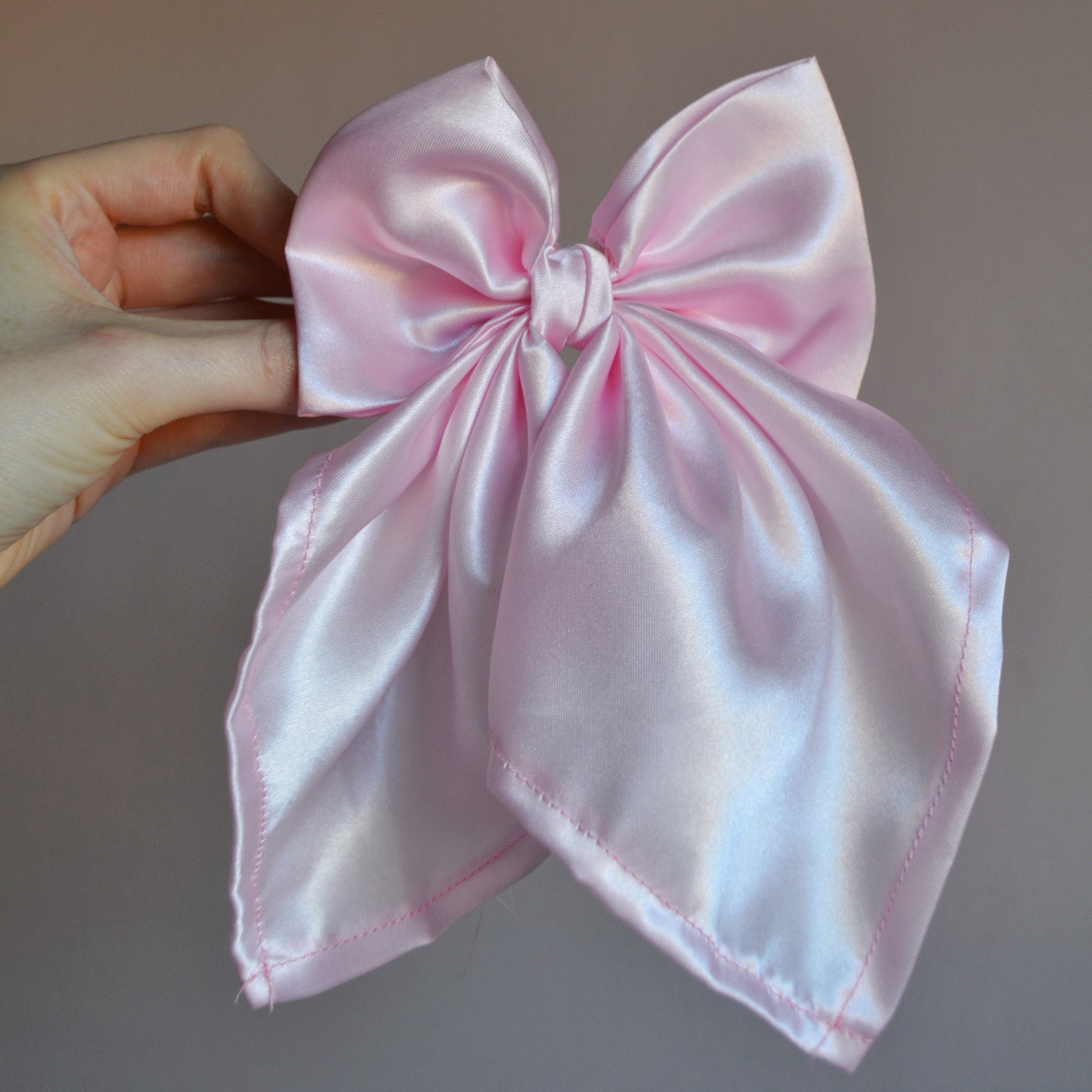 Pink satin bow held by a hand against a plain background