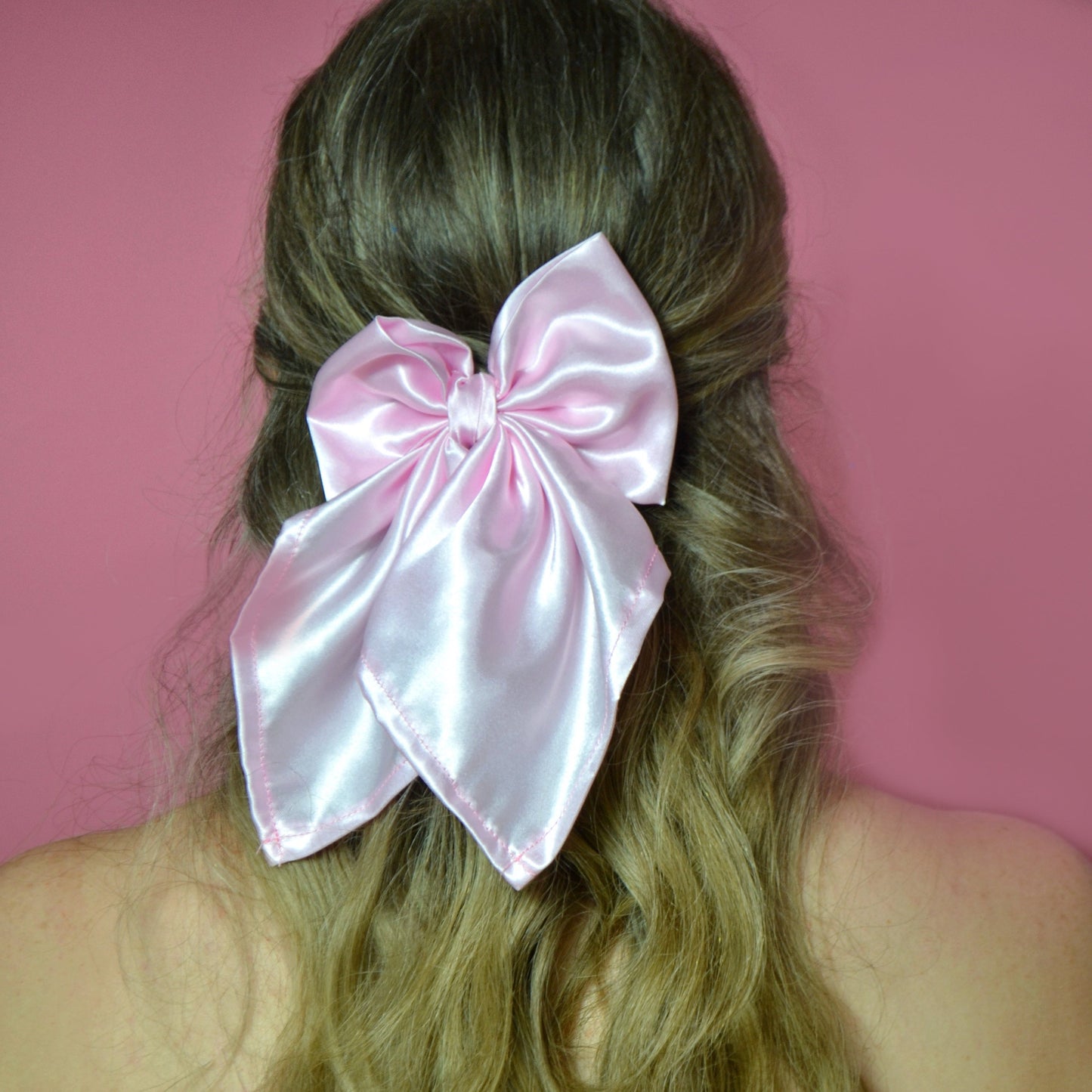 Person with long hair wearing a large pink satin bow against a pink 