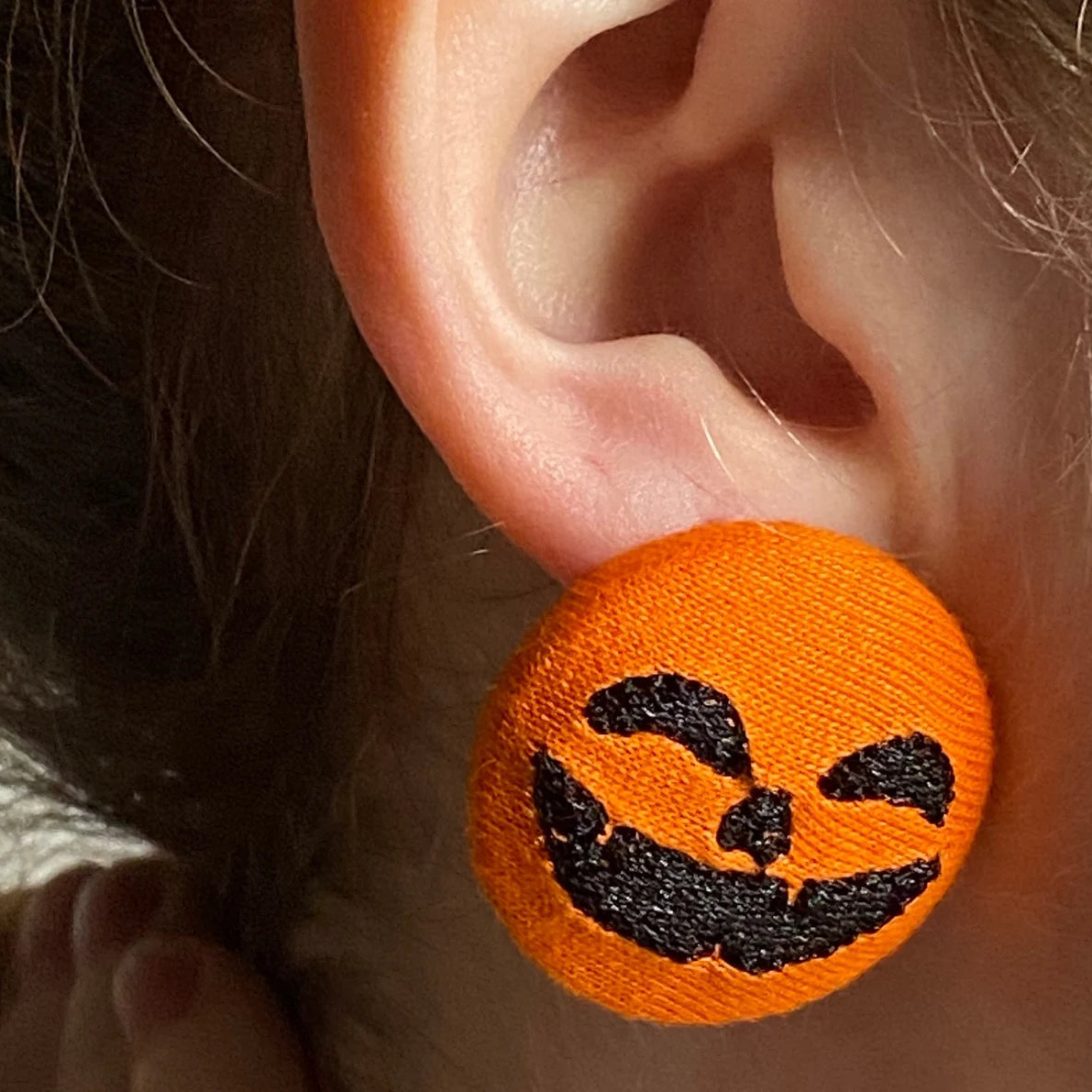 Extreme close-up of Halloween jack-o’-lantern earring showing embroidery detail, ideal for fall accessories.