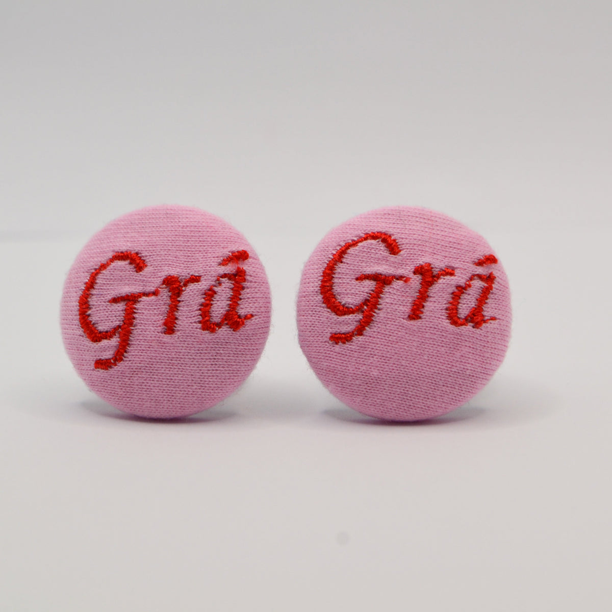 Pink Irish Gra earrings with red embroidered text on a light gray background